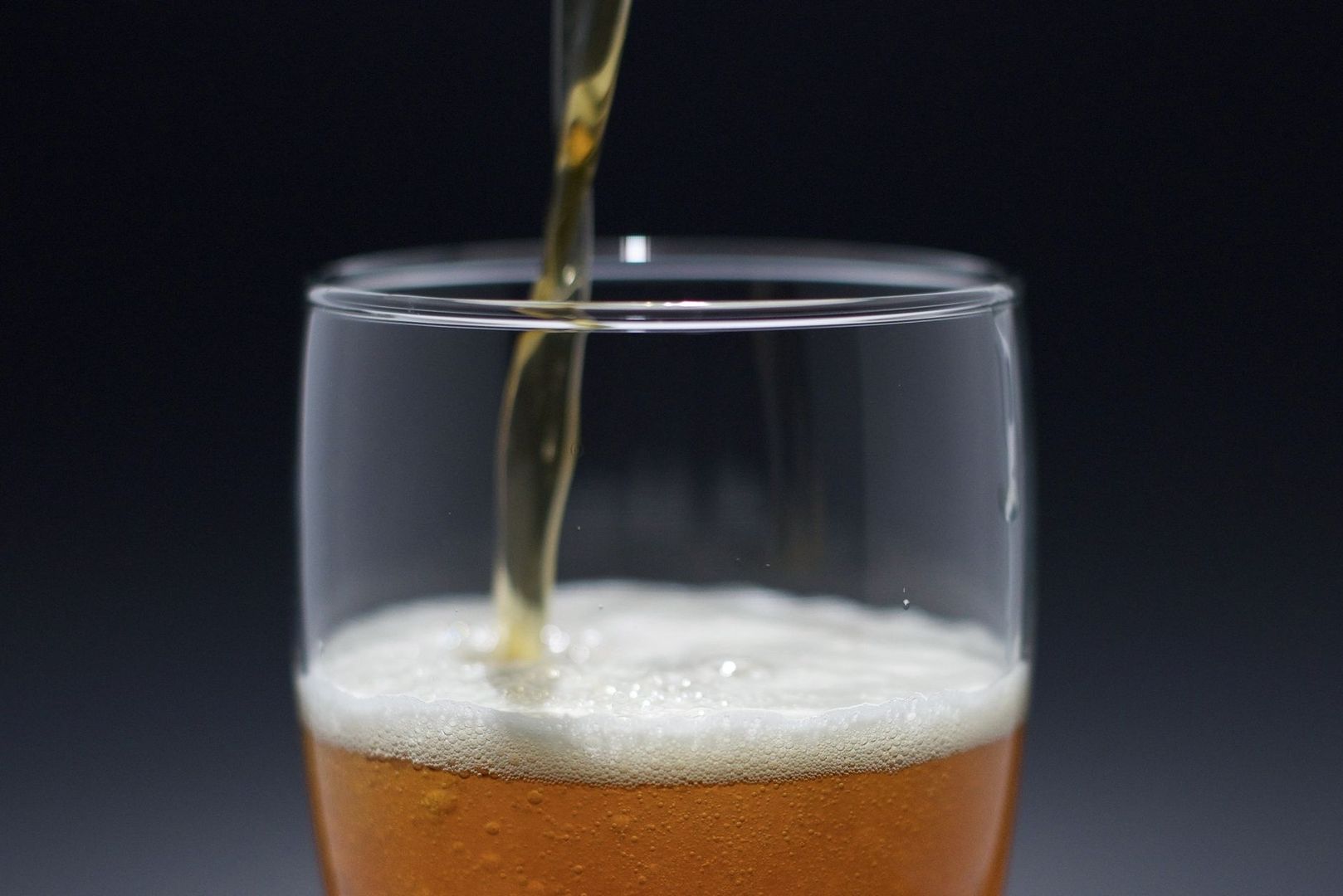 Golden cider being poured into a clear pint glass with foam